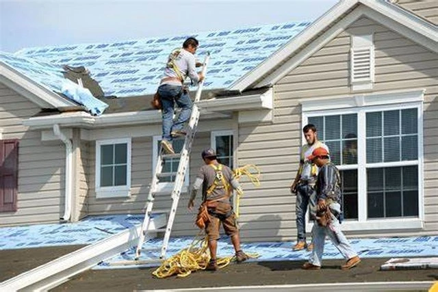 Picutre of four Roofing Contractors installing shingles on the main level of the home and the upper level of the home